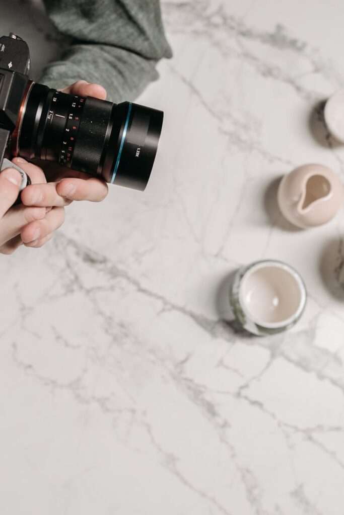Man photographing ceramic cups on marble surface from above, indoors.